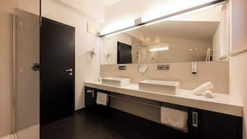 Un baño moderno con piso oscuro, un espejo grande, dos lavamanos y una zona de ducha.