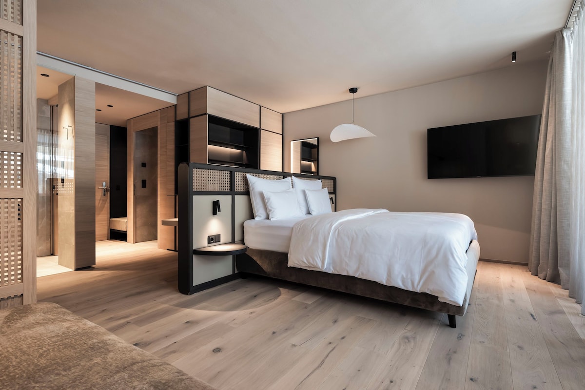 A modern bedroom with a bed, bedside tables, a TV, and a walk-in closet.