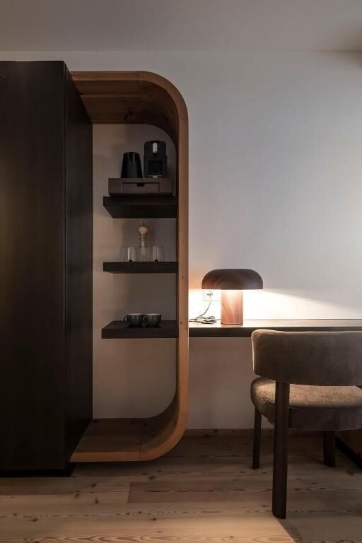 A modern room with a curved wooden cabinet, a desk with a lamp, and a chair.