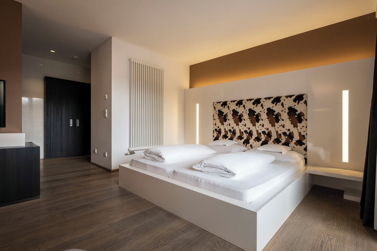 A modern bedroom with a large bed, a built-in headboard with a unique pattern, and a bedside table.