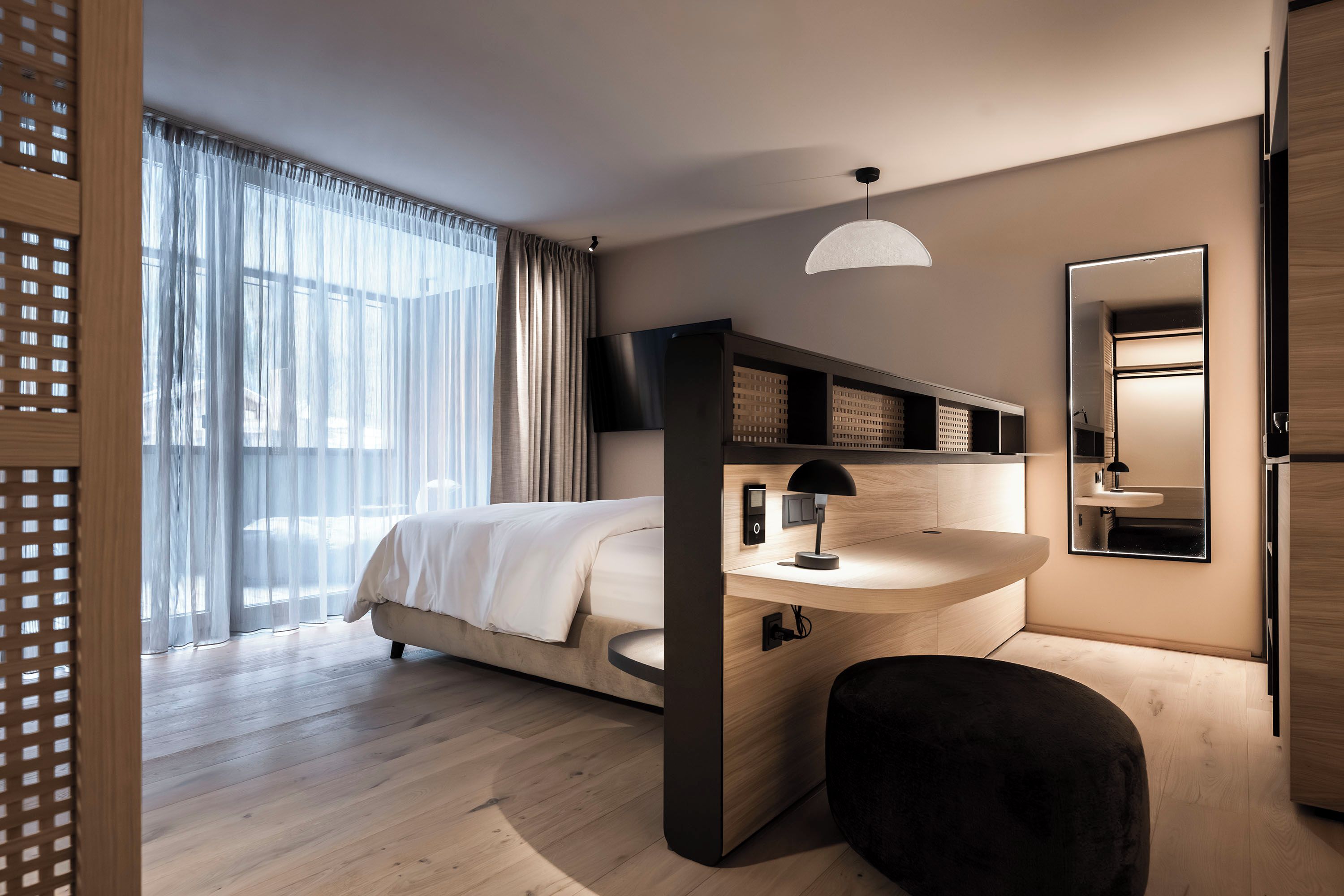 A modern hotel room with a bed, bedside table, lamp, and a large mirror.