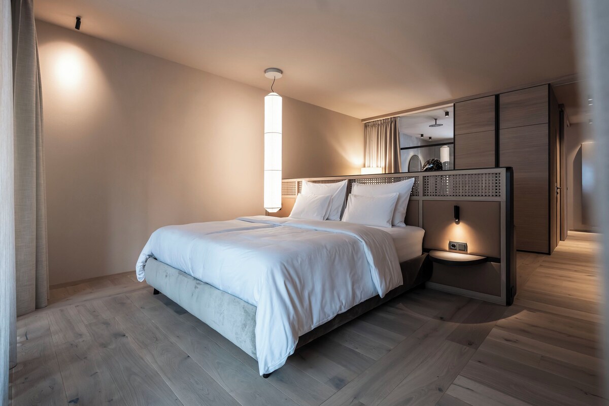 A modern bedroom with a large bed, a bedside table, a wall-mounted lamp, and a wardrobe.