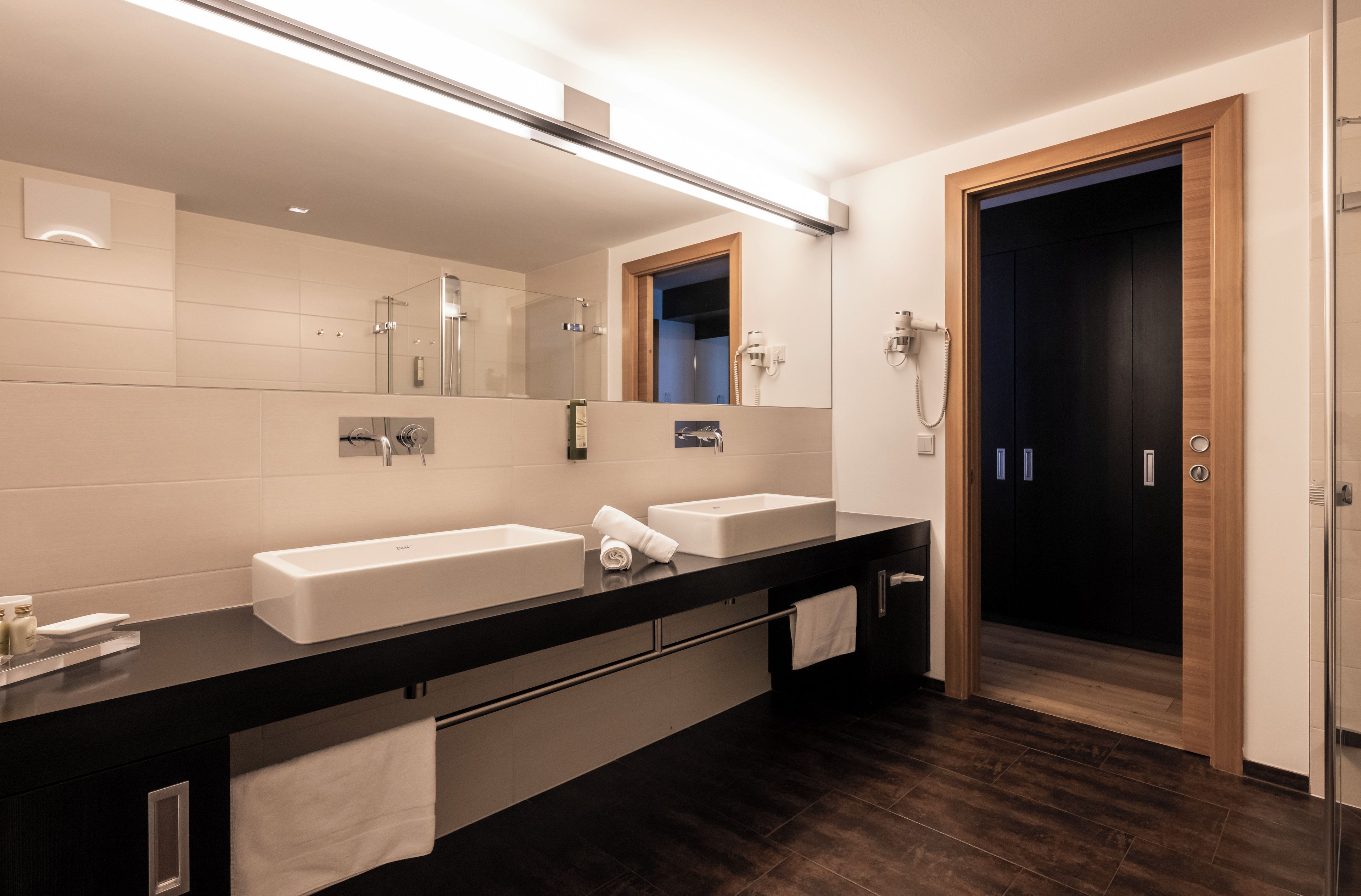 A modern bathroom with two sinks, a large mirror, and a shower.