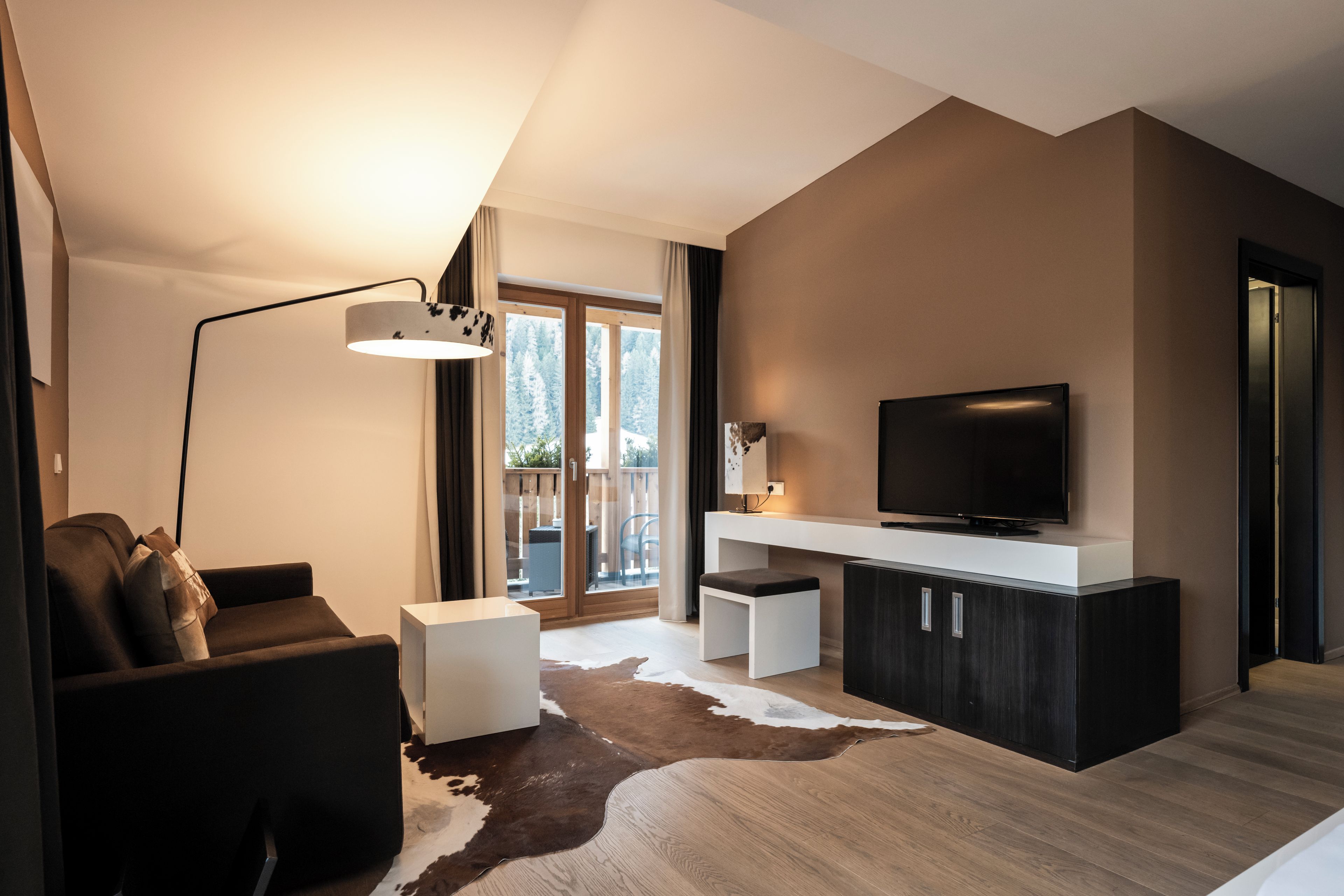 A modern living room with a flat-screen TV, a sofa, a coffee table, and a cowhide rug.