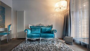 A room with a teal sofa, a patterned rug, a radiator, a chair, and a hanging light fixture.