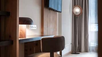 A room with a wooden desk, a chair, a television mounted on the wall, and a window with curtains.