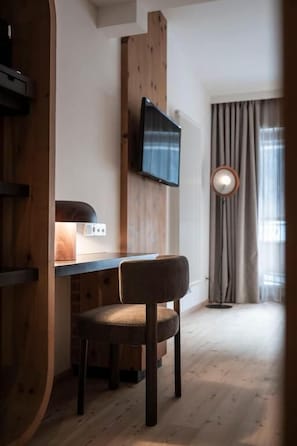 A room with a wooden desk, a chair, a television mounted on the wall, and a window with curtains. - Hotel Monika - Adults Only (Sesto)