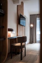 Una habitación con un escritorio de madera, una silla, un televisor montado en la pared y un ventanal con cortinas.
