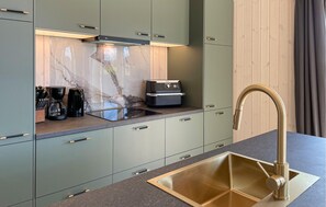A modern kitchen with a built-in oven, a coffee maker, and a sink with a gold faucet. - Nice home in Væggerløse with sauna (Væggerløse)
