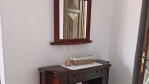 A wooden console table with a mirror above it, a wicker basket, and a small shelf with books.