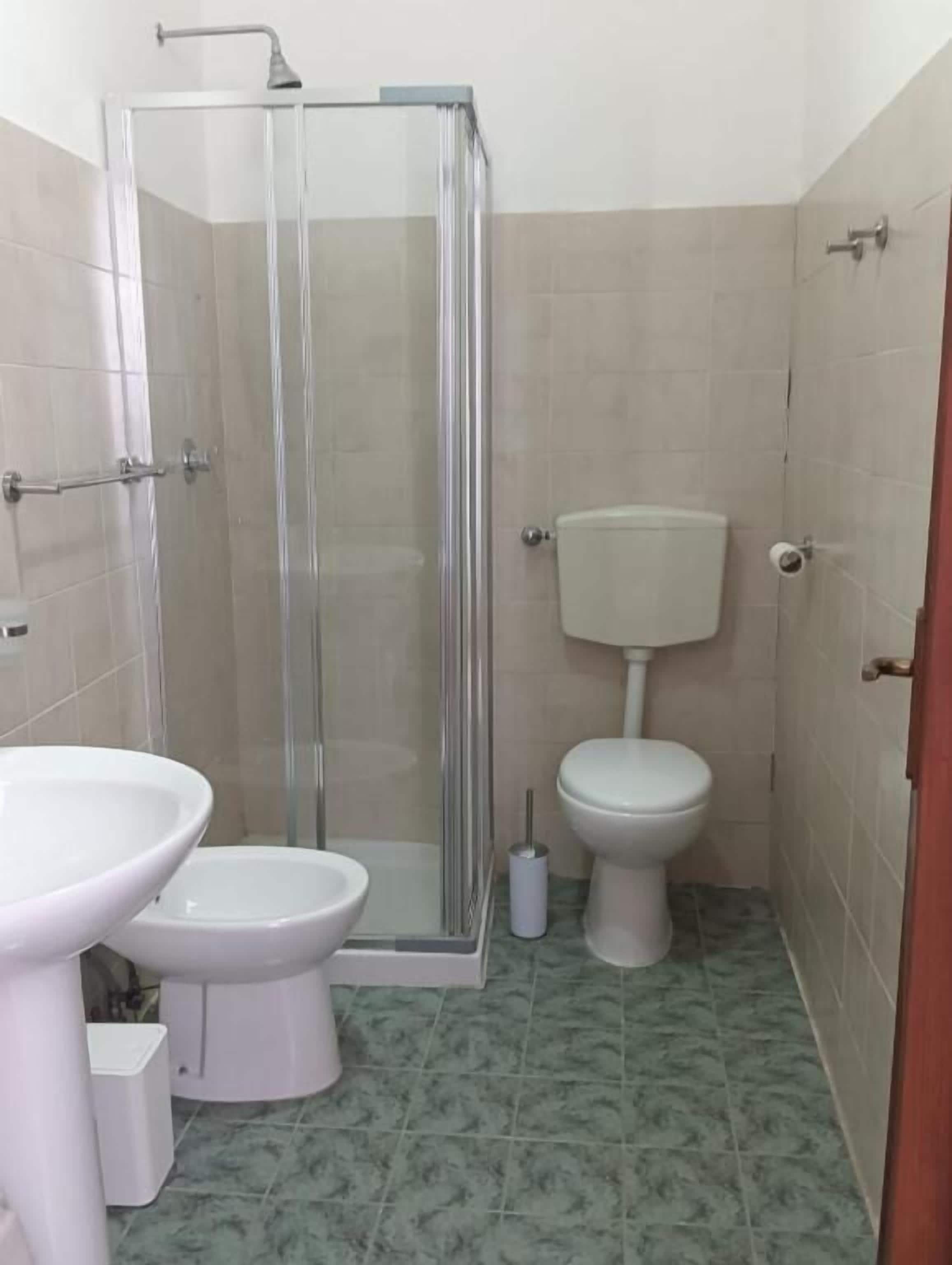 A bathroom with a glass-enclosed shower, a toilet, and a sink.