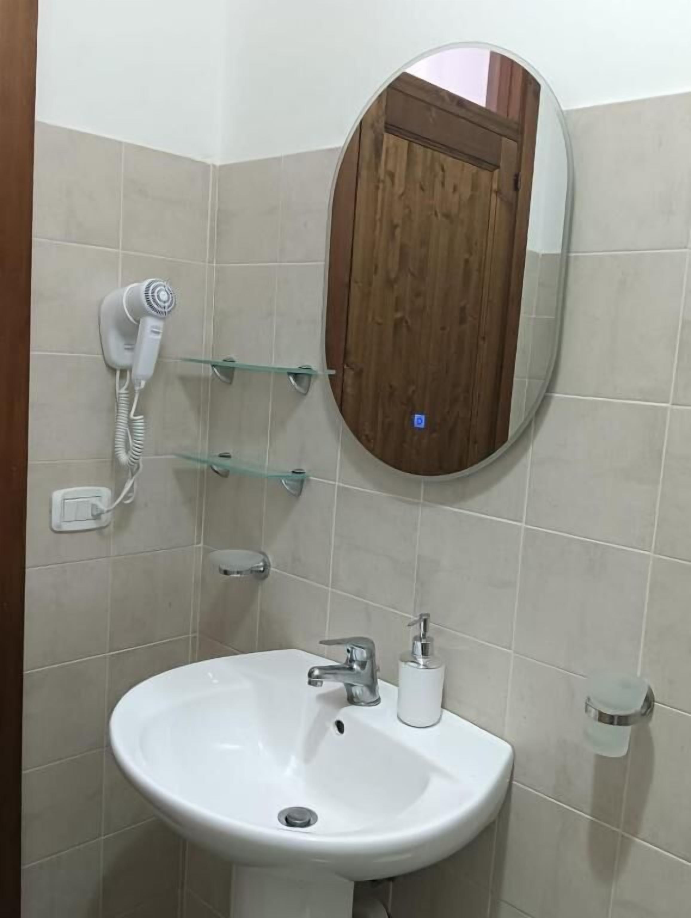Un baño con lavamanos blanco, un espejo, un secador de pelo y una puerta de madera.