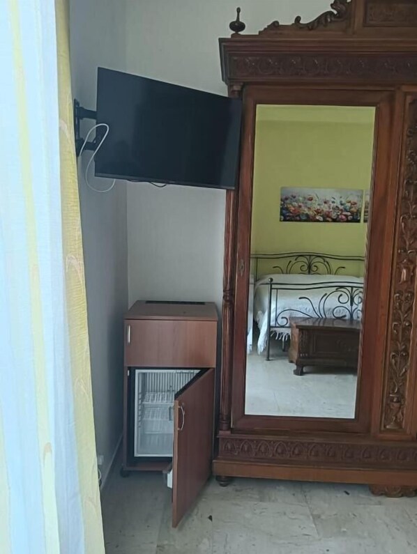 Una habitación con cama, armario, televisor y un refrigerador pequeño.