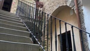 A staircase with a metal railing leading to an upper level, surrounded by stone walls and a door at the bottom.
