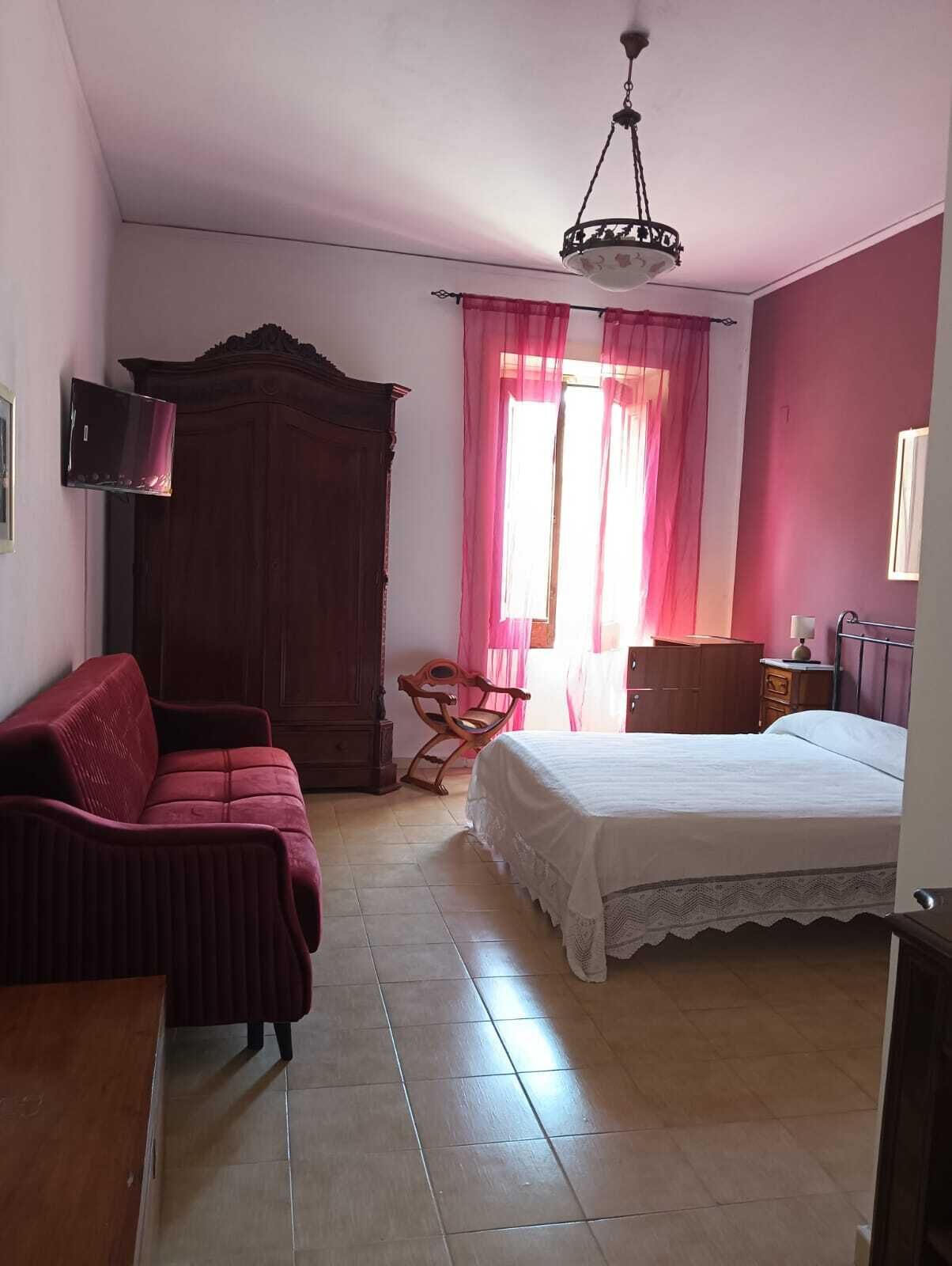 Una camera da letto con un letto, un'armadio in legno, una poltrona rossa, una sedia e una televisione a parete.