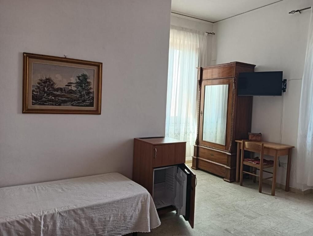 A room with a bed, a wooden cabinet, a television, and a painting on the wall.