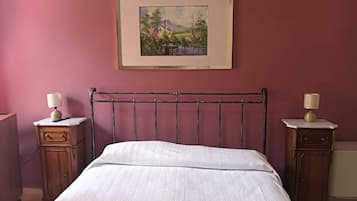 Una camera da letto con un letto singolo, un comodino con una lampada, una cassettiera e un quadro con un paesaggio appeso al muro.