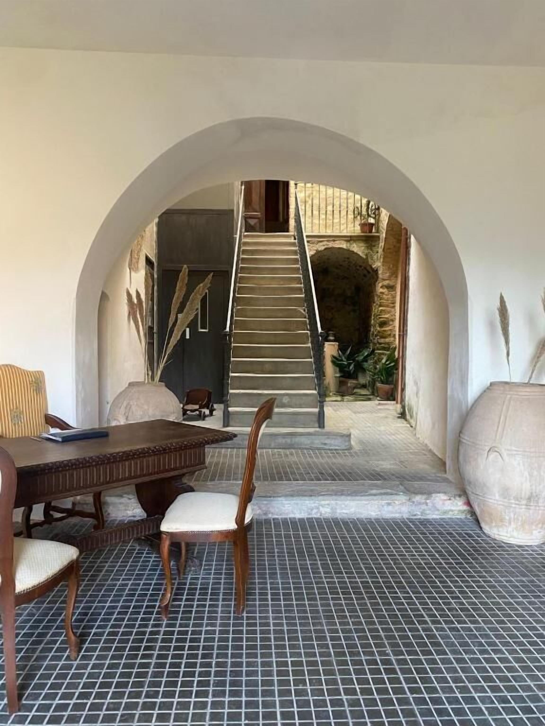 Ein Innenraum mit Esstisch und Stühlen, einem rundbogigen Durchgang zu einer Treppe und einem Fliesenboden.