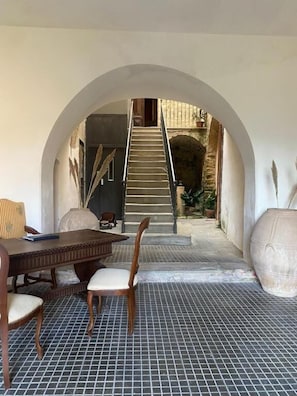 Un espacio interior con una mesa de comedor y sillas, un arco que da a una escalera y un suelo de baldosas.