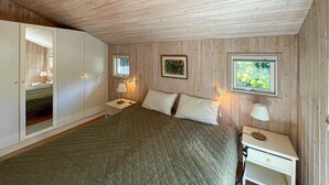 Une chambre à coucher avec un lit, deux tables de chevet, une fenêtre et un téléviseur fixé au mur.