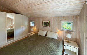 Ein Schlafzimmer mit einem Bett, zwei Nachttischen, einem Fenster und einem an der Wand montierten Fernseher.