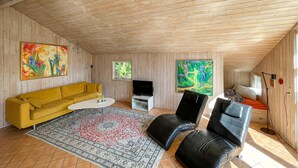 Une pièce avec un canapé jaune, une table basse blanche, un fauteuil en cuir noir, un téléviseur et des œuvres d’art accrochées aux murs.