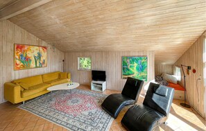 Ein Zimmer mit einem gelben Sofa, einem weißen Couchtisch, einem schwarzen Ledersessel, einem Fernseher und Kunstwerken an den Wänden.