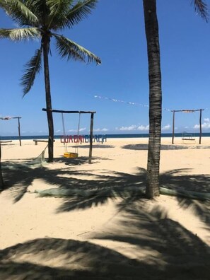 A beach with palm trees, a swing set, and a clear sky. - Coral Riverside Homestay & Hostel (Da Nang)