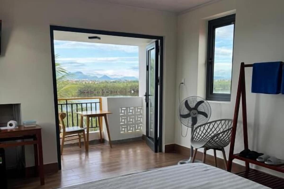 A room with a bed, a table, a chair, a fan, and a view of the outdoors.