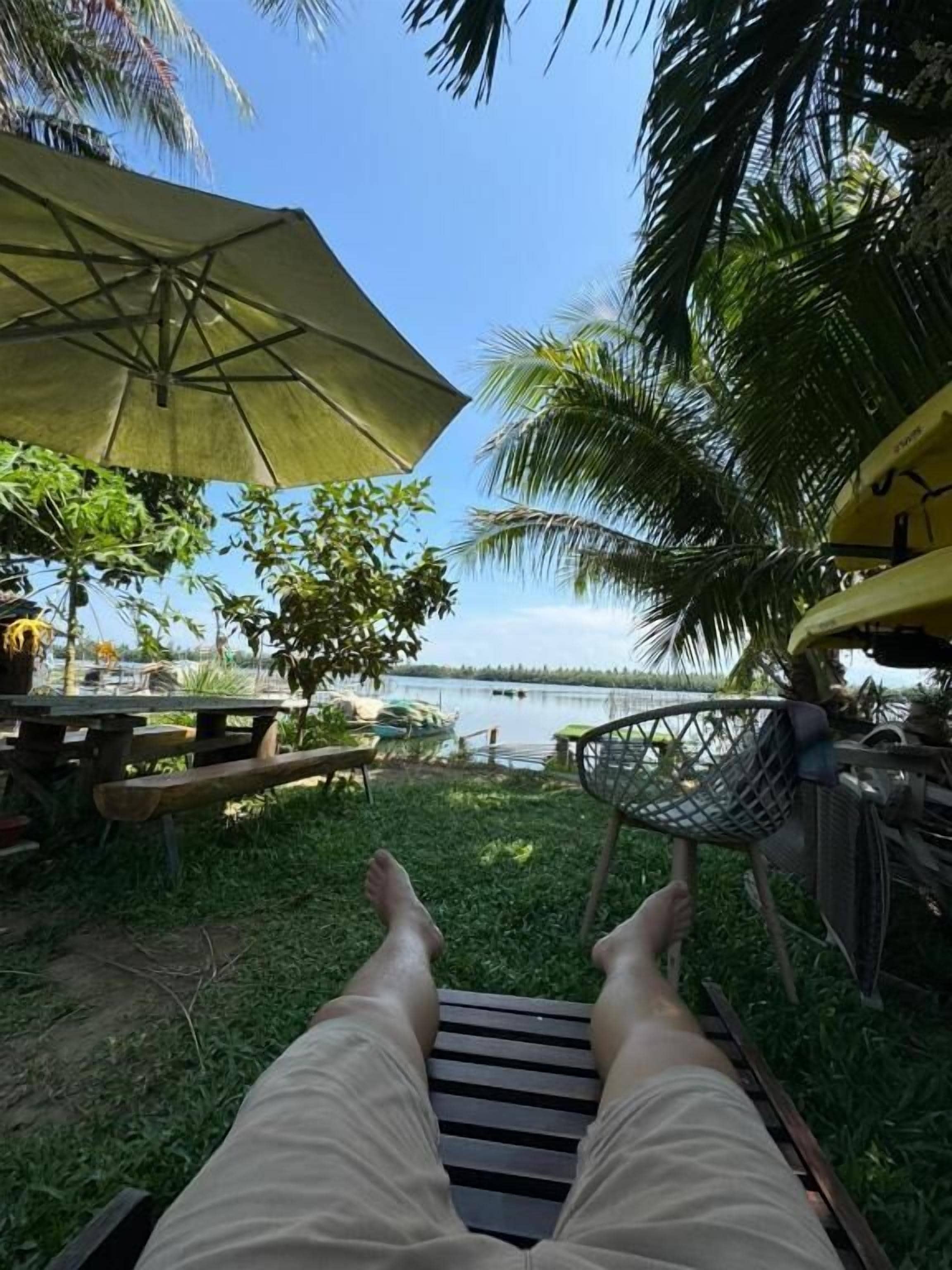 Una persona recostada en un banco con vista a un lago y palmeras.