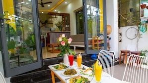 An outdoor dining area with a table set for two, a vase of flowers, and a variety of dishes and drinks.