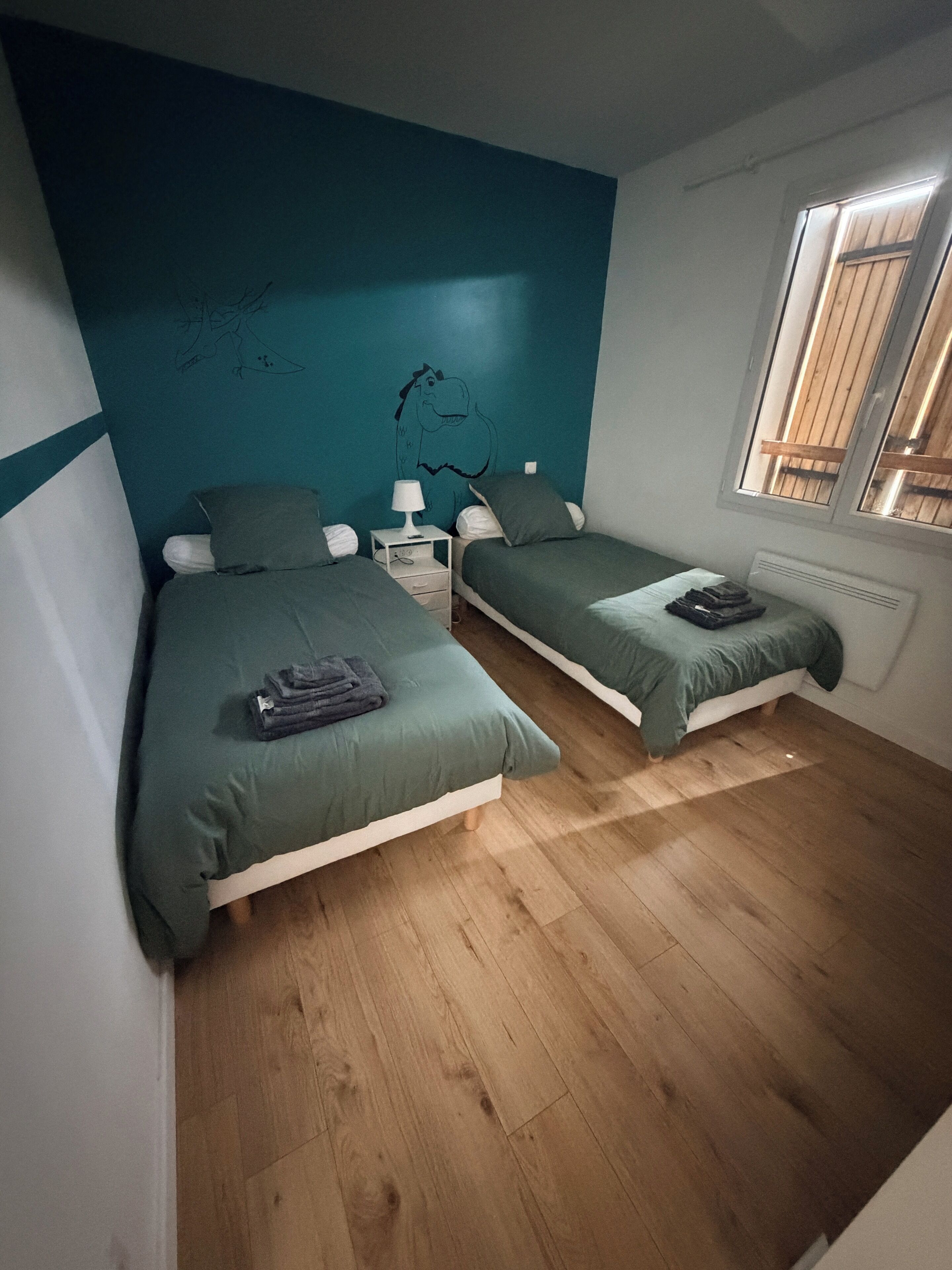 A bedroom with two single beds, a nightstand, a lamp, and a window with wooden shutters.