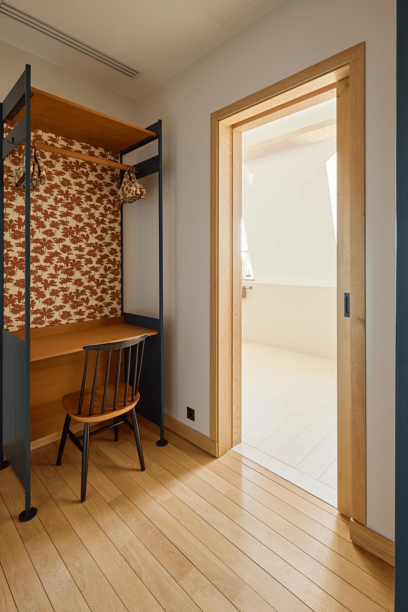 A room with a bunk bed, a chair, a wooden desk, and a door leading to an outdoor area.