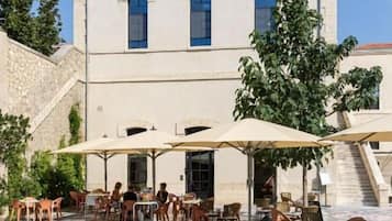 Un bâtiment à la façade en pierre, doté d’un espace extérieur avec des tables et des parasols, ainsi que d’un chemin en pierre.