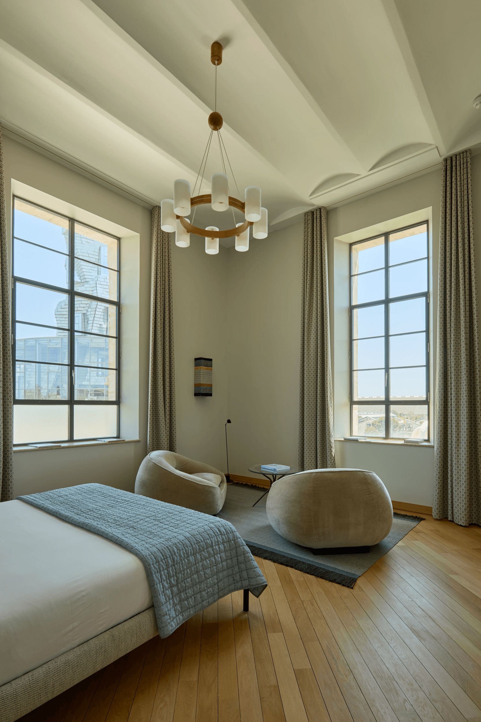 Un dormitorio con una cama grande, una zona de estar circular y dos ventanas con cortinas.