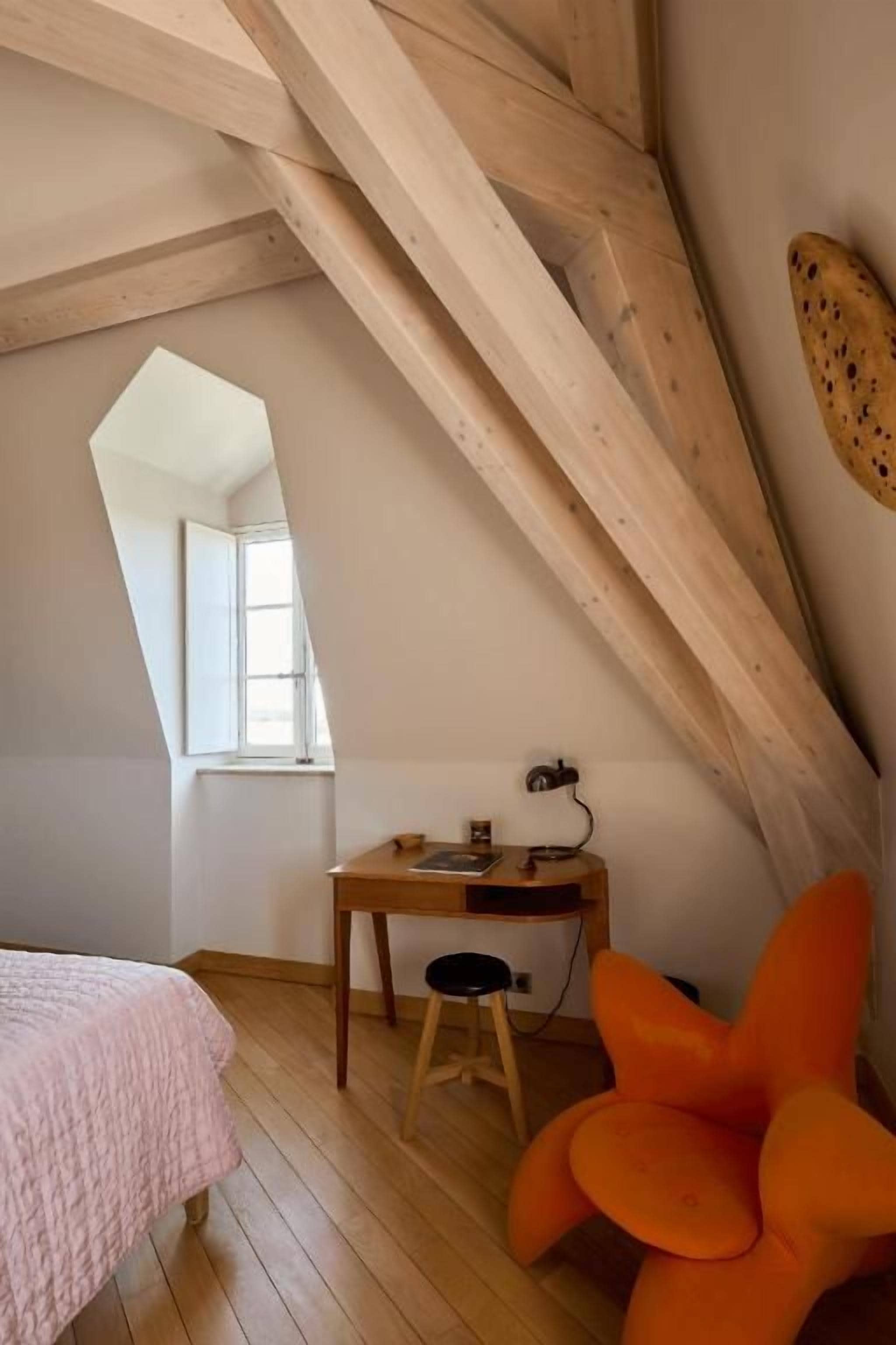A room with a sloped ceiling, a bed, a desk with a chair, and a window.