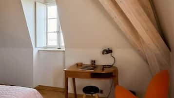 Une pièce avec un plafond en pente, un lit, un bureau avec une chaise et une fenêtre.