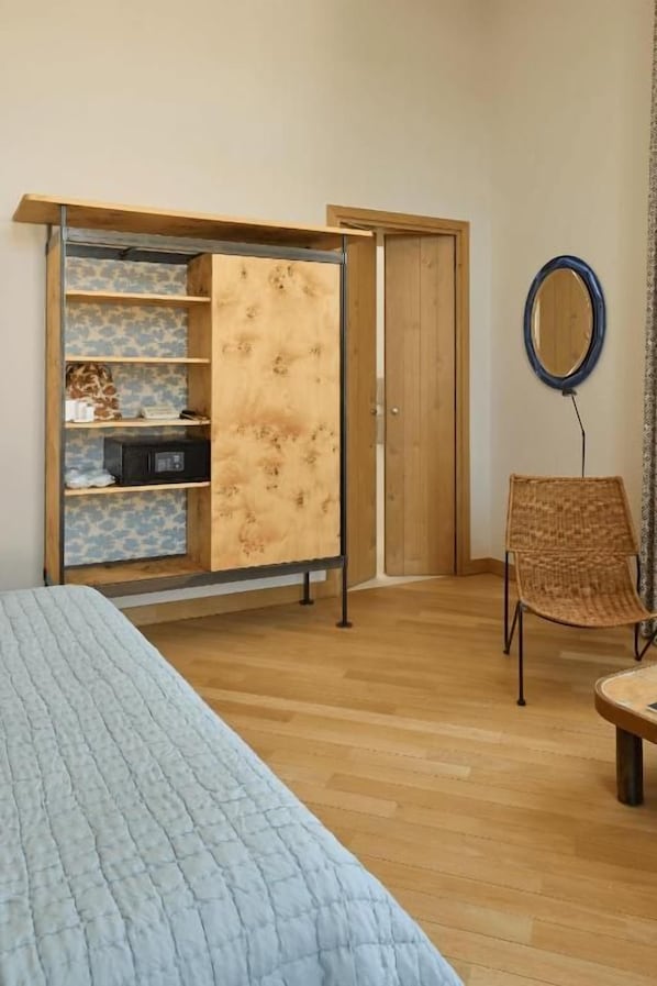 A bedroom with a bed, a wardrobe with shelves, a chair, and a round mirror on the wall.