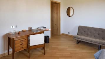 A room with a wooden desk, a grey sofa, a wooden door, and a round mirror on the wall.
