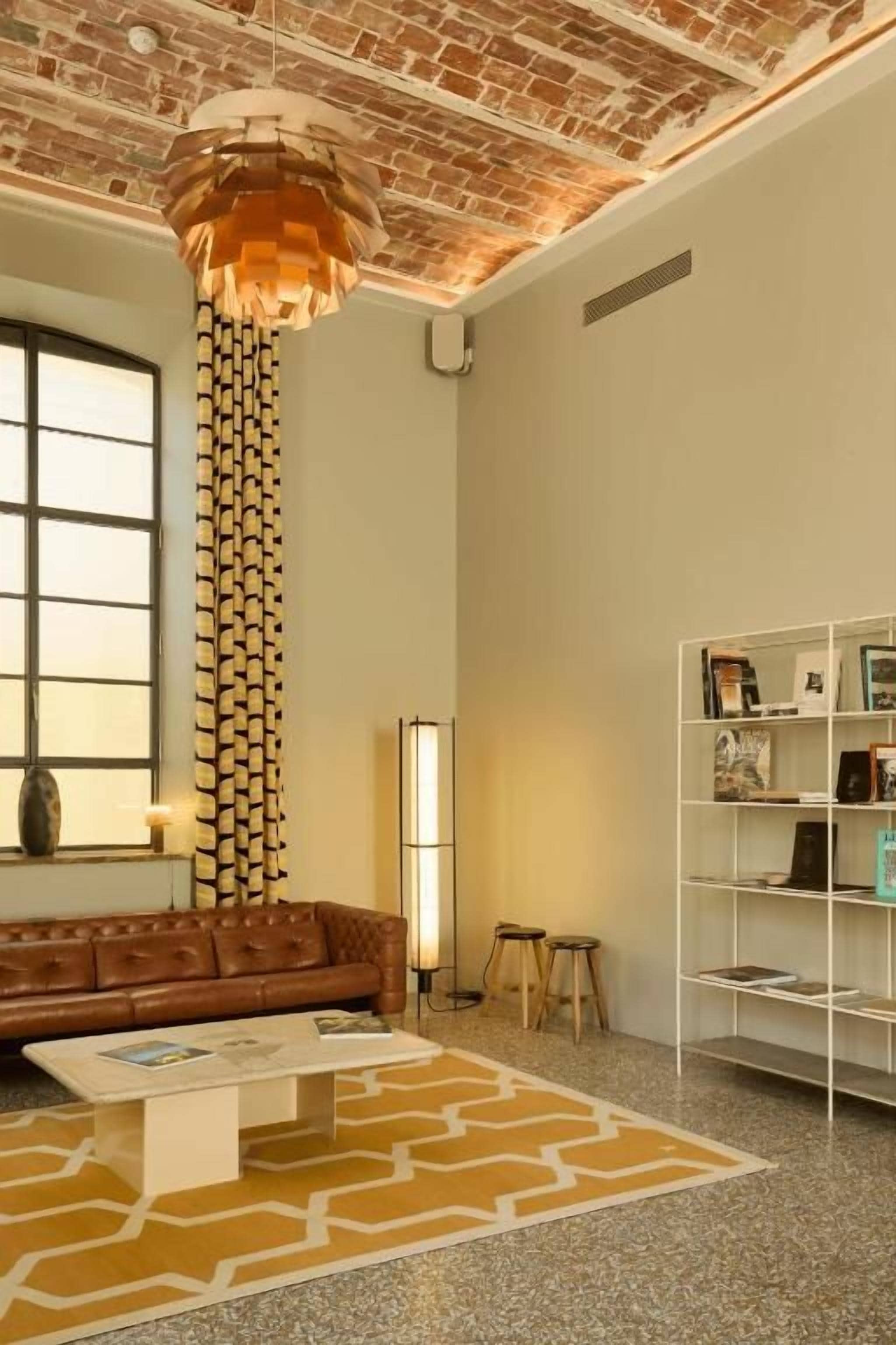 A room with a brick ceiling, a brown leather sofa, a white coffee table, a patterned rug, and a bookshelf.