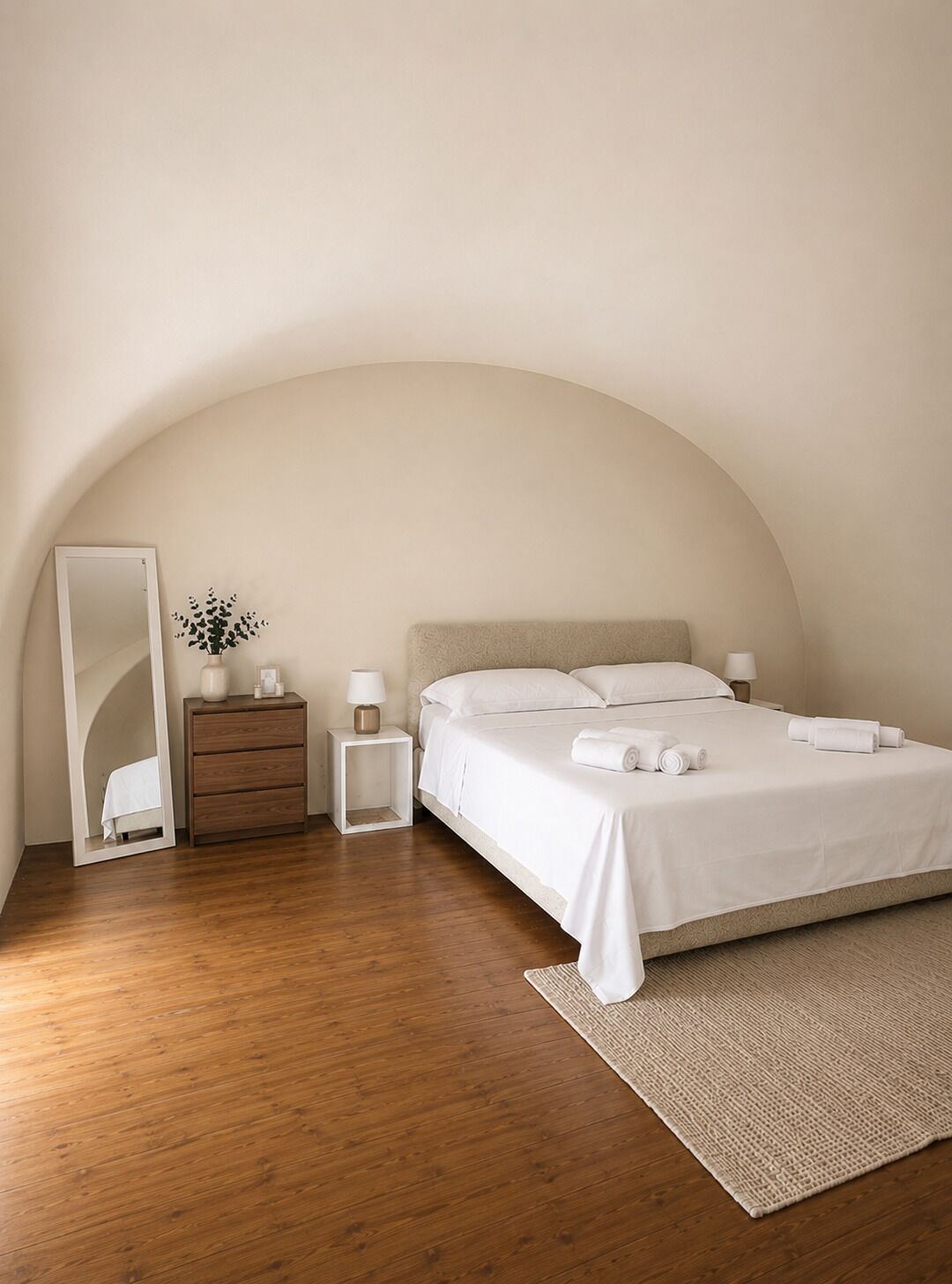 A bedroom with a bed, bedside tables, a mirror, and a wooden floor.