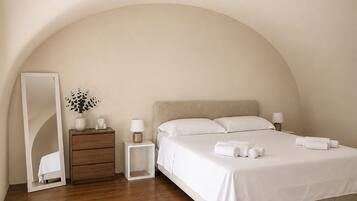 A bedroom with a bed, bedside tables, a mirror, and a wooden floor.