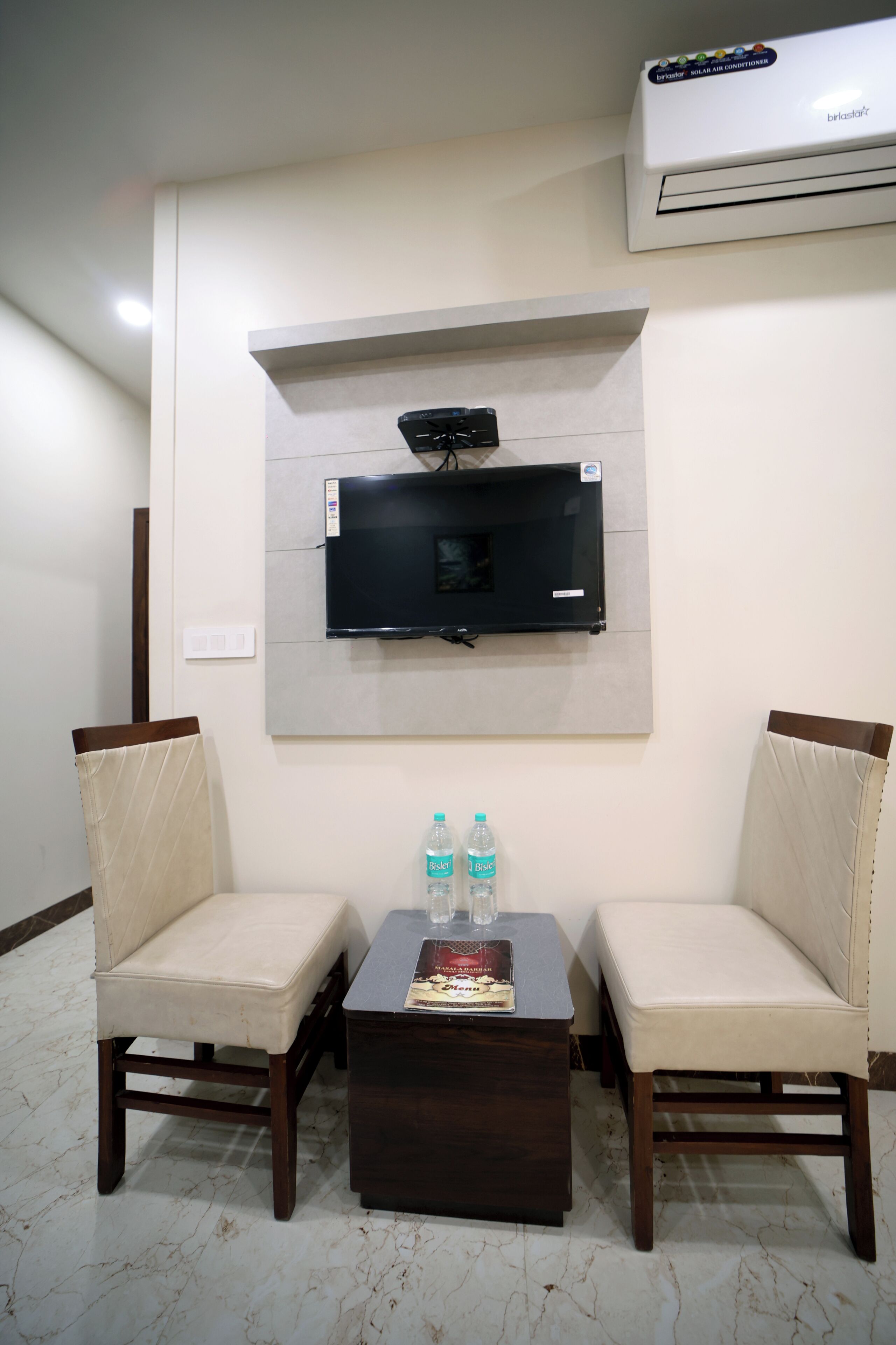 Una habitación con dos sillas, una mesa, un televisor de pantalla plana montado en la pared y un aire acondicionado en el techo.