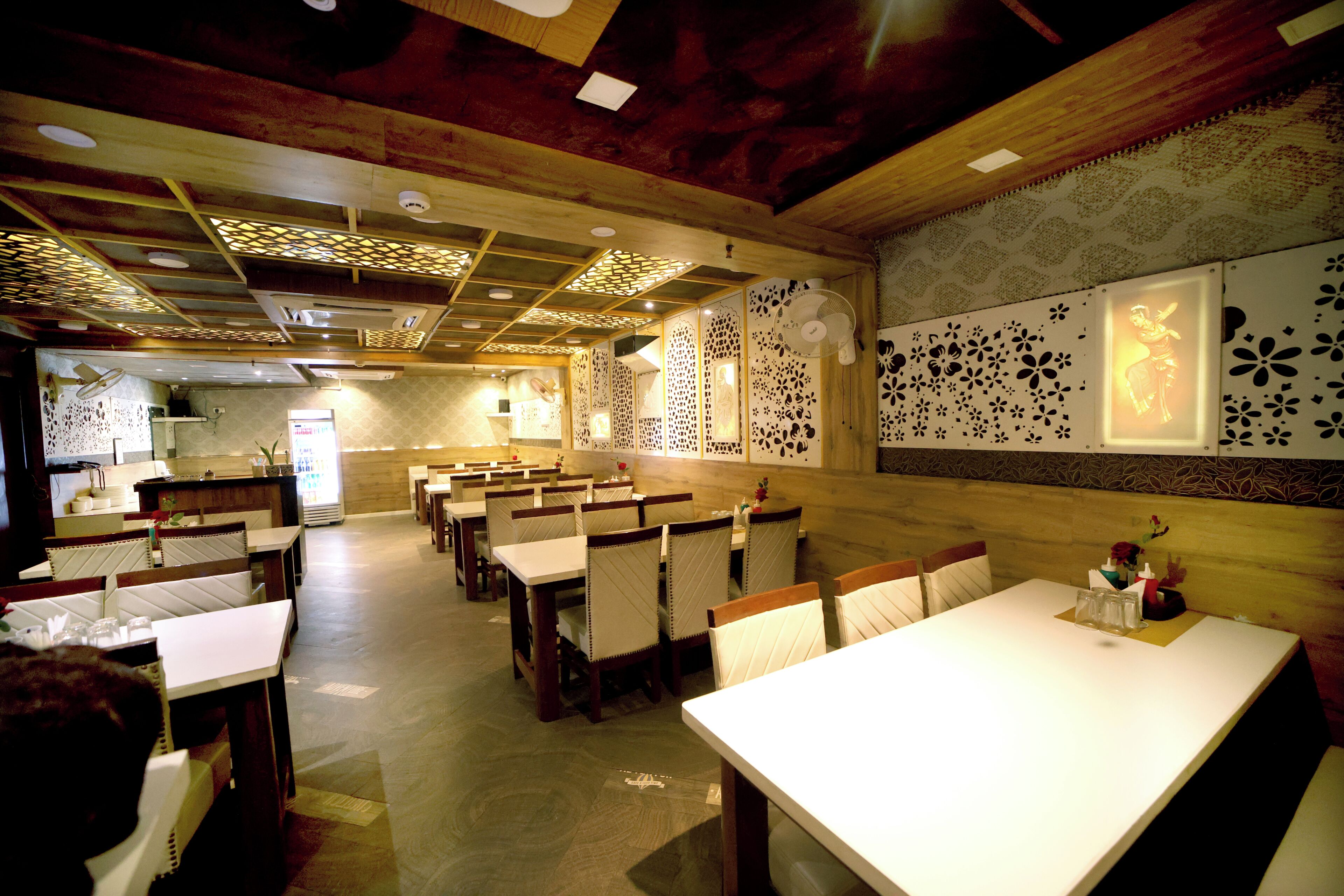 Interior de restaurante con techo de madera, decoraciones de pared con diseños y varias mesas de comedor con sillas.