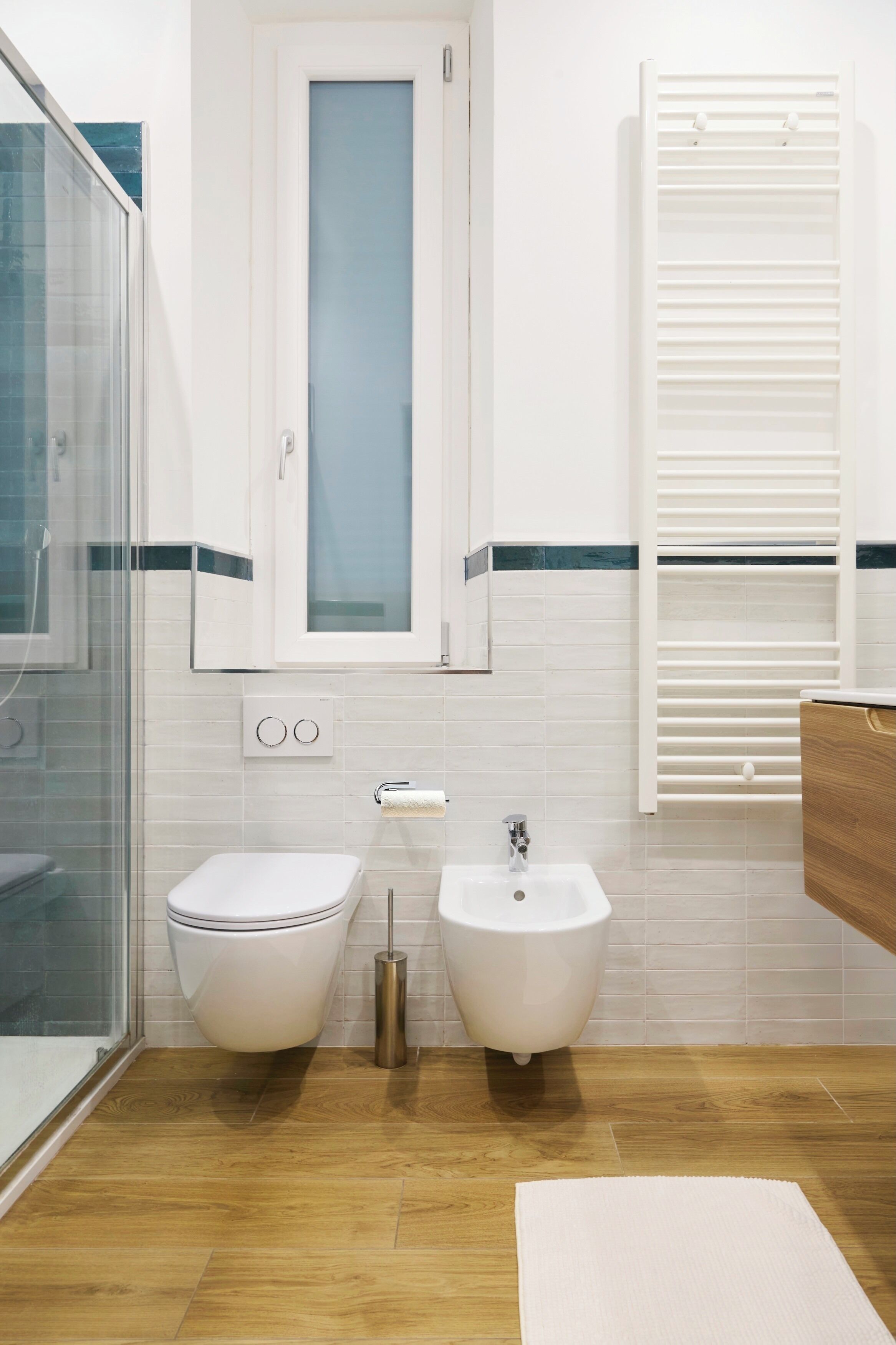 Un baño con cabina de ducha de vidrio, inodoro blanco, bidé y suelo de madera.