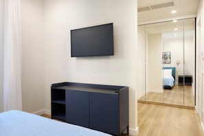 Ein Schlafzimmer mit einem Bett, einem an der Wand montierten Fernseher, einem Kleiderschrank und einer Schranktür mit Spiegel.