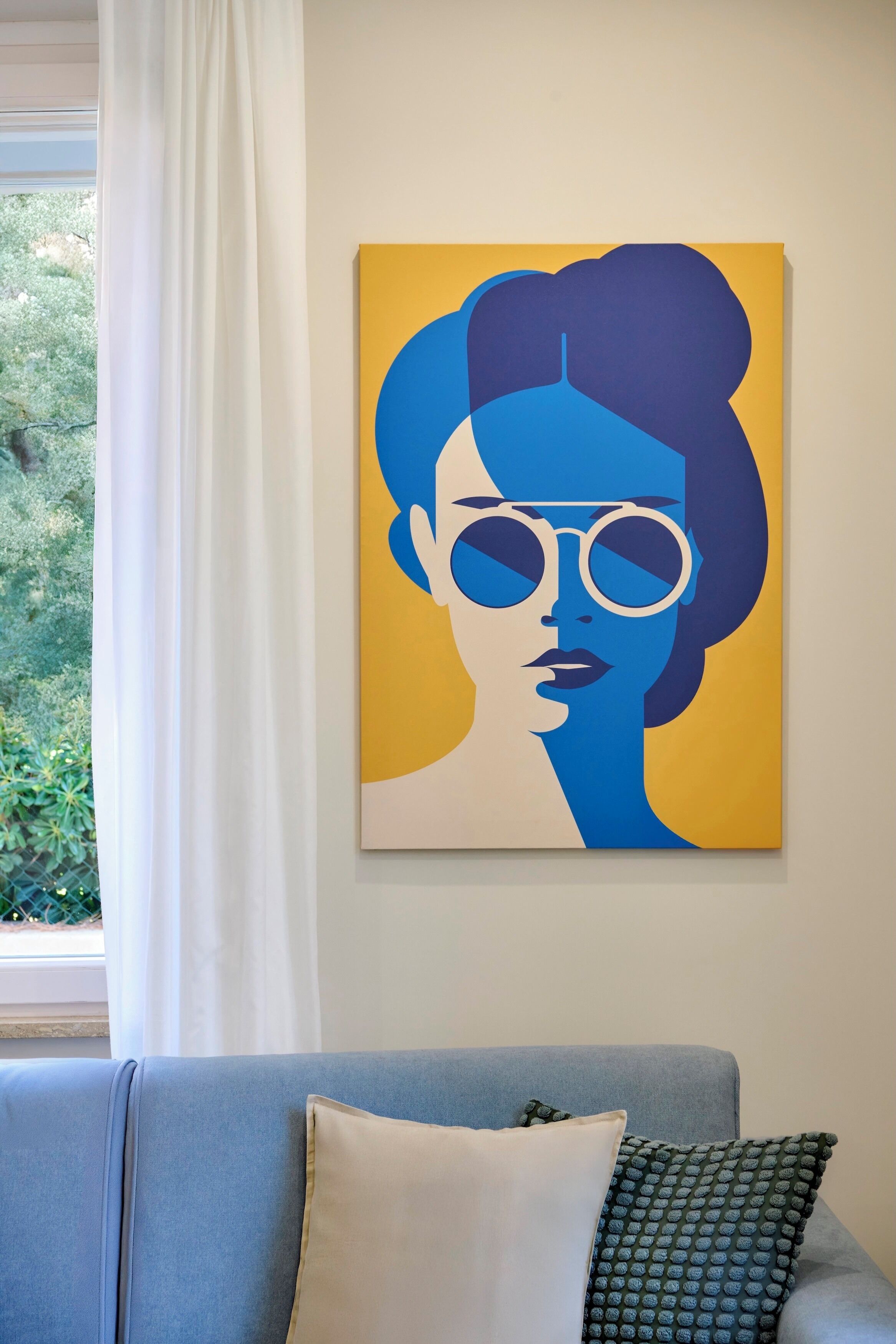 A room with a blue sofa, a white pillow, and a yellow and blue artwork on the wall.