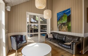 A modern living room with a leather sofa, a round white table, and a glass door leading to an outdoor area. - Beautiful home in Blåvand with sauna (Blåvand)