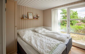 A bedroom with a bed, a window, and a shelf with framed pictures. - Beautiful home in Blåvand with sauna (Blåvand)