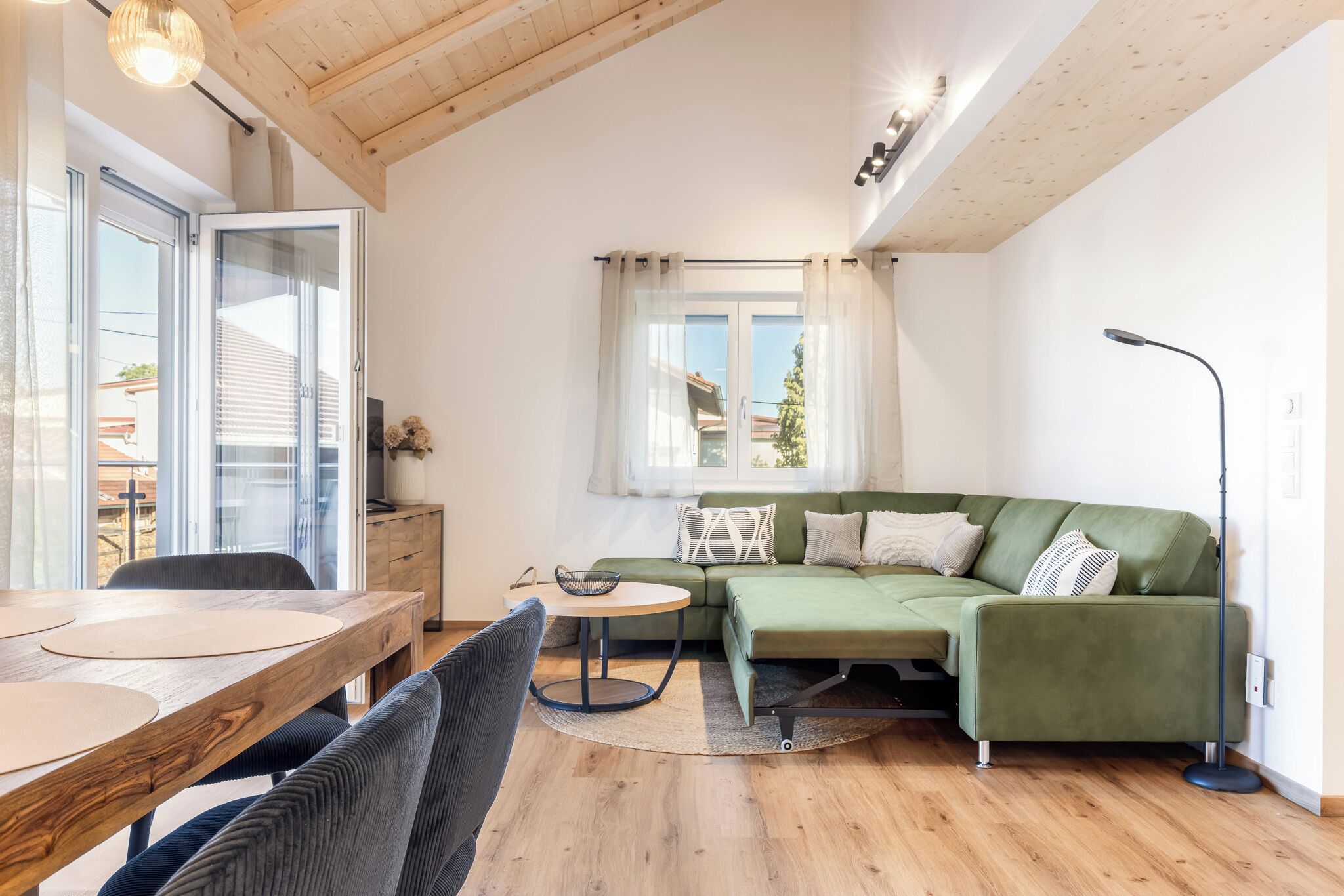 A modern living room with a wooden dining table, a green sofa, and a small round table.